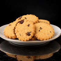KimBeA stack of golden-brown baked apricot biscuits with dark raisin pieces, served on a white ceramic plate with a thin gold rim, set against a dark reflective background.