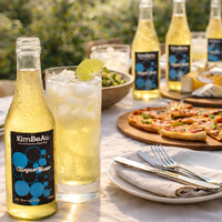 Buy Online KimBeAu premium ginger beer fiery cocktail mixer, a refreshing beverage that will awaken your senses."served with ice and lime at outdoor lunch table
