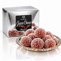 A silver metallic box labeled KimBeau Guava Cheese sits behind a decorative silver plate piled with round, sugar-coated guava cheese balls on a white reflective background.
